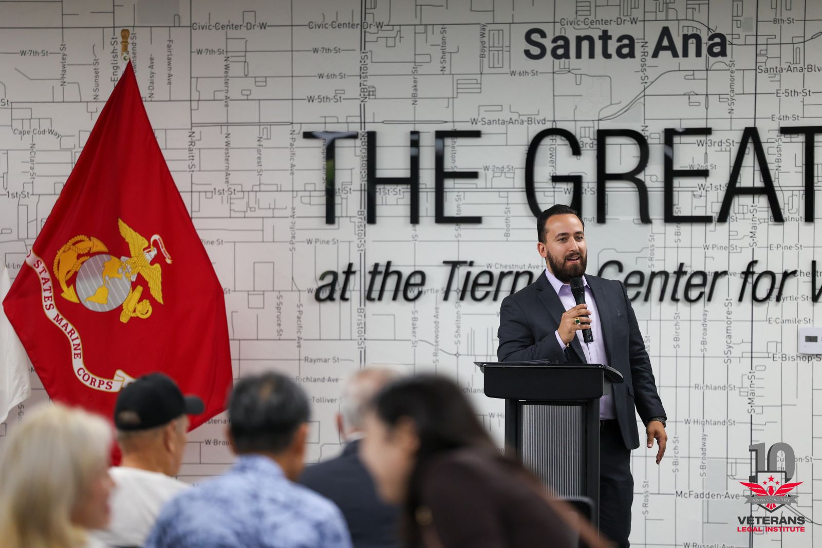 James Burandt speaking at a podium beside a Marine Corps flag before an audience